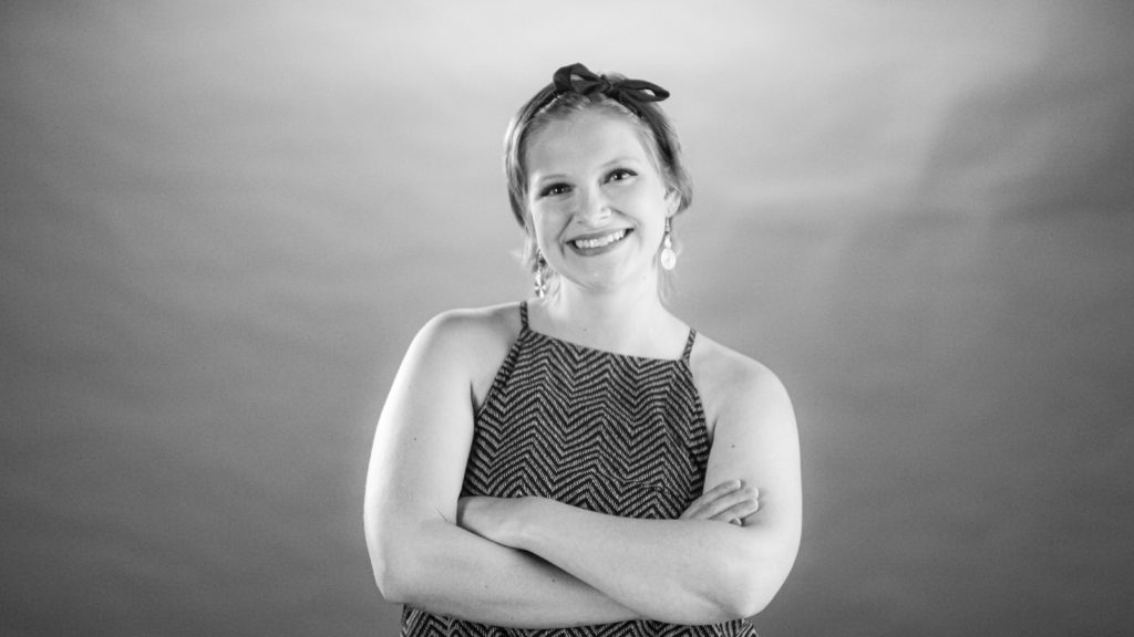 Young adult woman smiling and crossing her arms in front of a backdrop